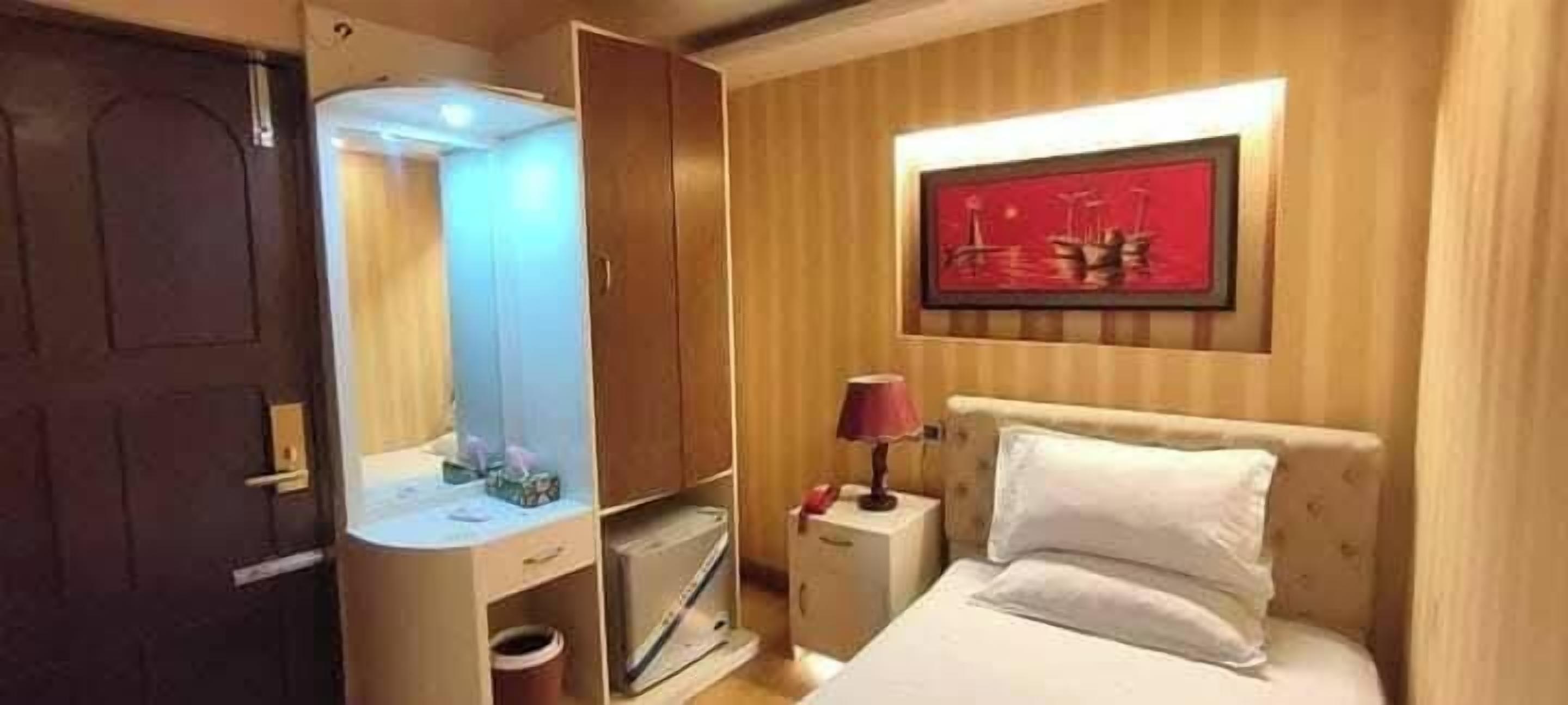 A hotel room with a bed, a nightstand, a lamp, a wardrobe, and a framed picture on the wall.