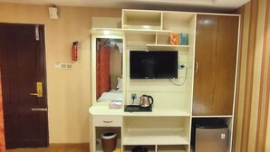 Een kamer met een televisie, planken, een waterkoker, een prullenbak en een deur.