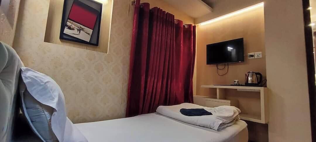 Una habitación de hotel con cama, televisión montada en la pared, cafetera y cortina roja.
