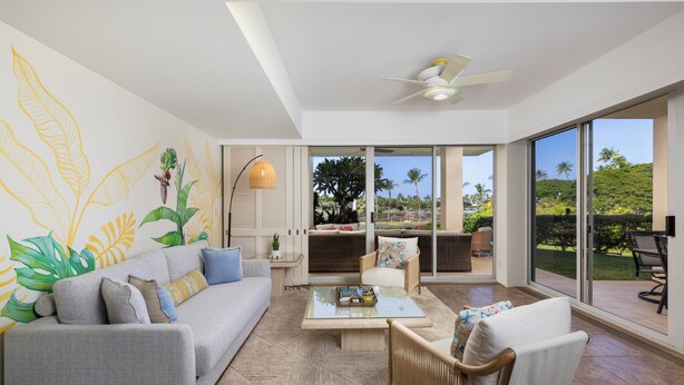 A modern living room with a sofa, armchairs, a coffee table, and a large window with a view of greenery. - New! Stylish island living, walk to beach, opp to Hilton! Partial ocean views! (Waikoloa Village)