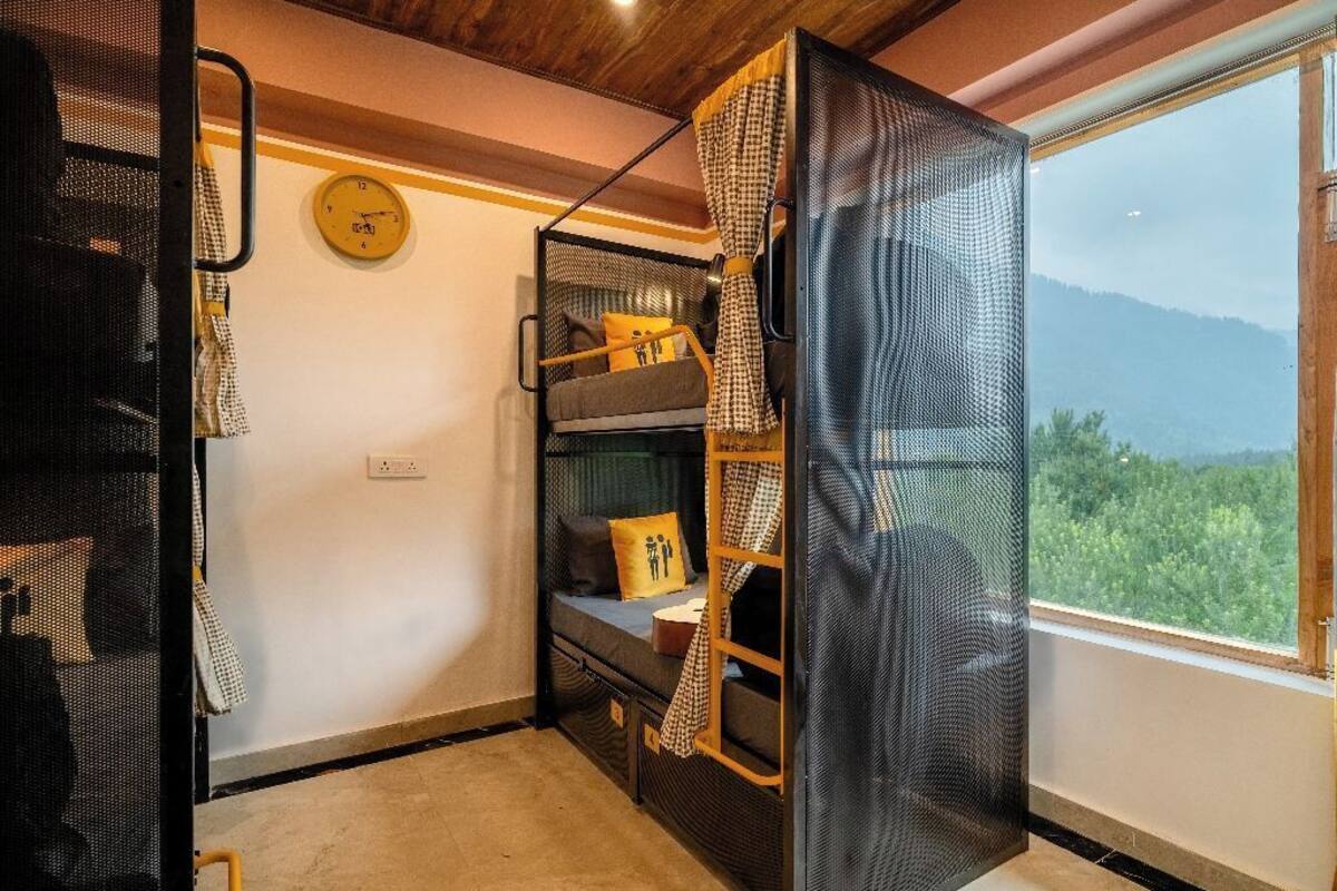 A compact room with bunk beds, a clock on the wall, and a window with a view of greenery.