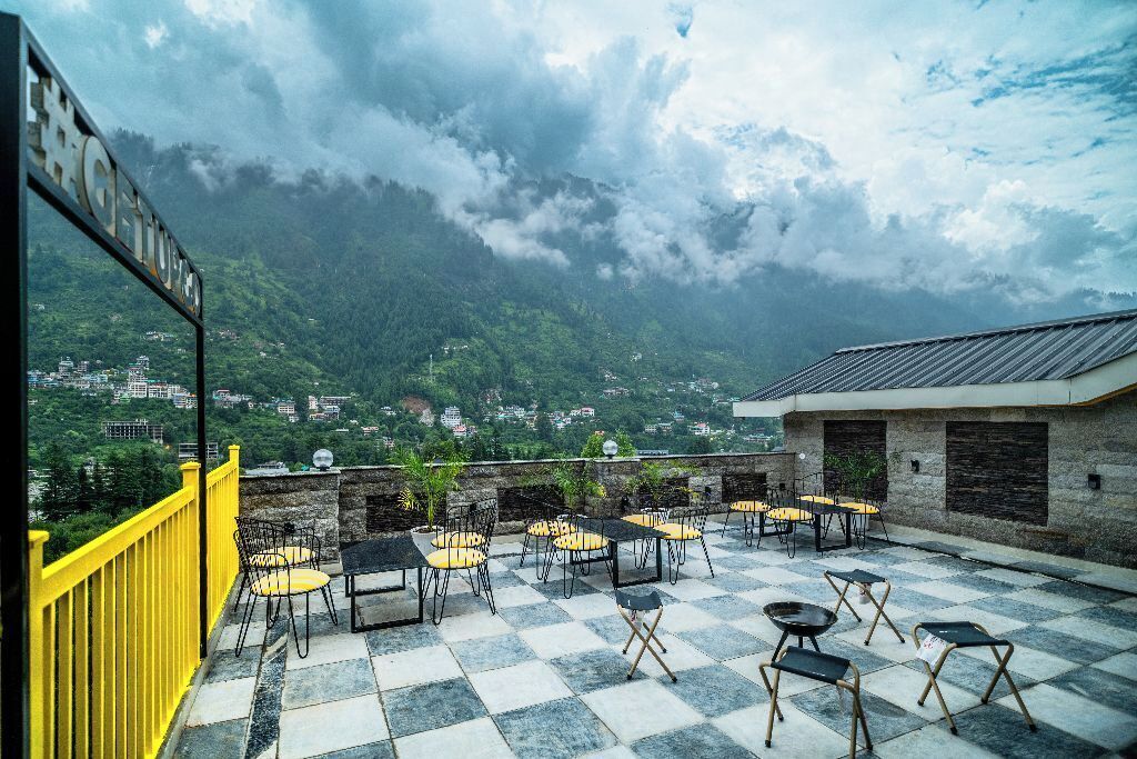 A terrace with checkered flooring, outdoor seating, and a view of a mountainous landscape.