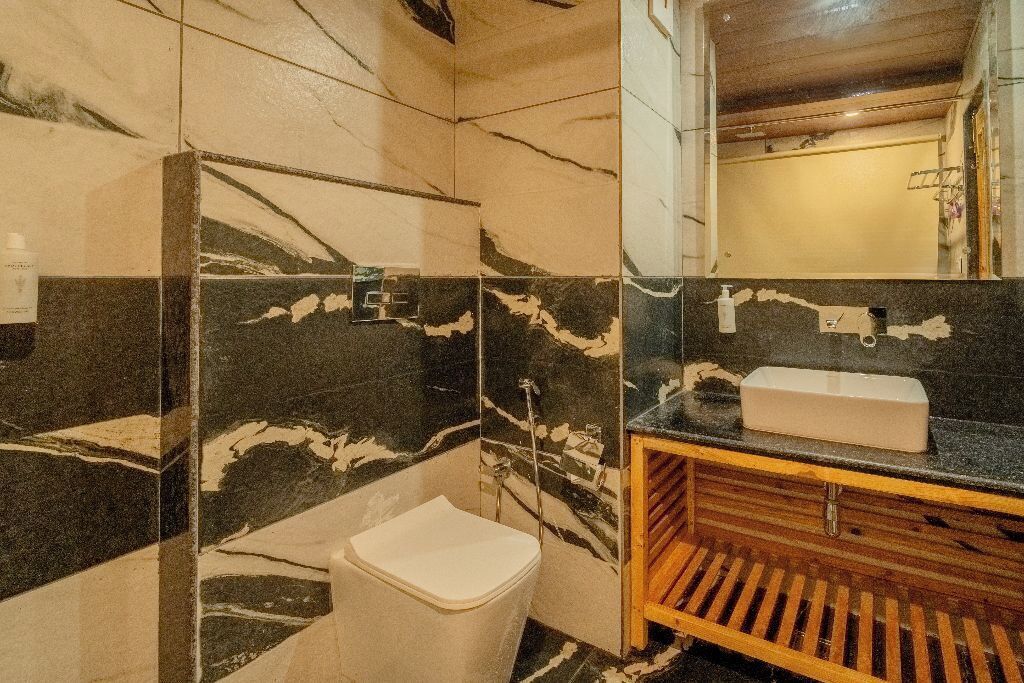 A bathroom with a marble wall, a white toilet, a wooden vanity, and a mirror.