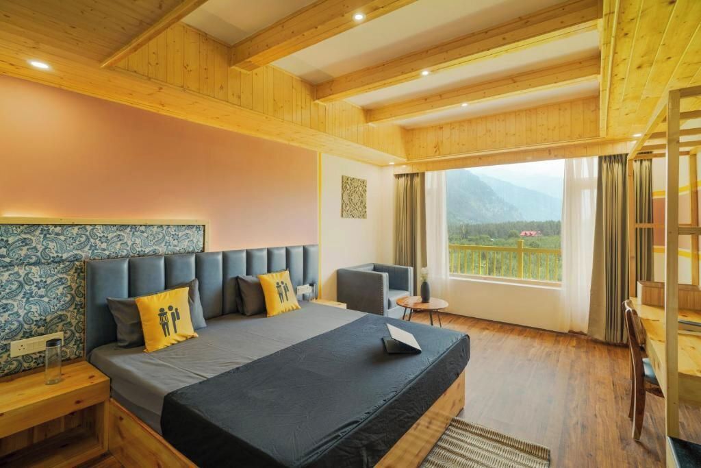 A bedroom with a large bed, a headboard with a blue and white pattern, a view of the outdoors through a window, and wooden ceiling beams.