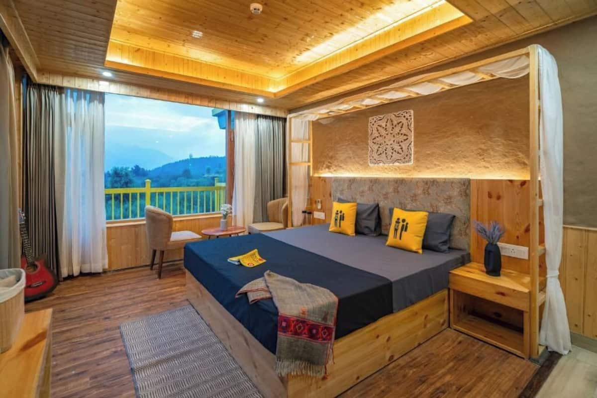 A wooden bedroom with a large bed, a view of the outdoors, and a small table with a chair.