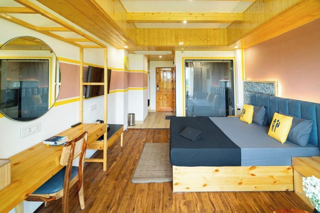 A bedroom with a wooden ceiling, a bed with blue bedding, a desk with a chair, and a large mirror.