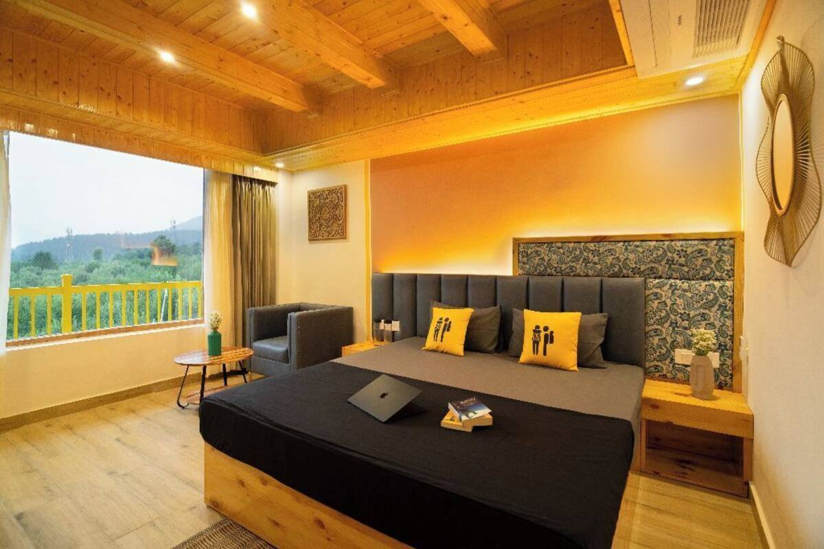 A bedroom with a bed, a desk, a chair, a window with a view, and a bedside table.