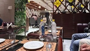 A restaurant with wooden tables and chairs, a decorative wall with yellow balloons, and a green vertical garden. - Rosewood Manali (Manali)