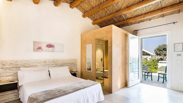Een moderne slaapkamer met een groot bed, een houten hoofdbord, een douchecabine met glazen wanden en een balkon met stoelen.