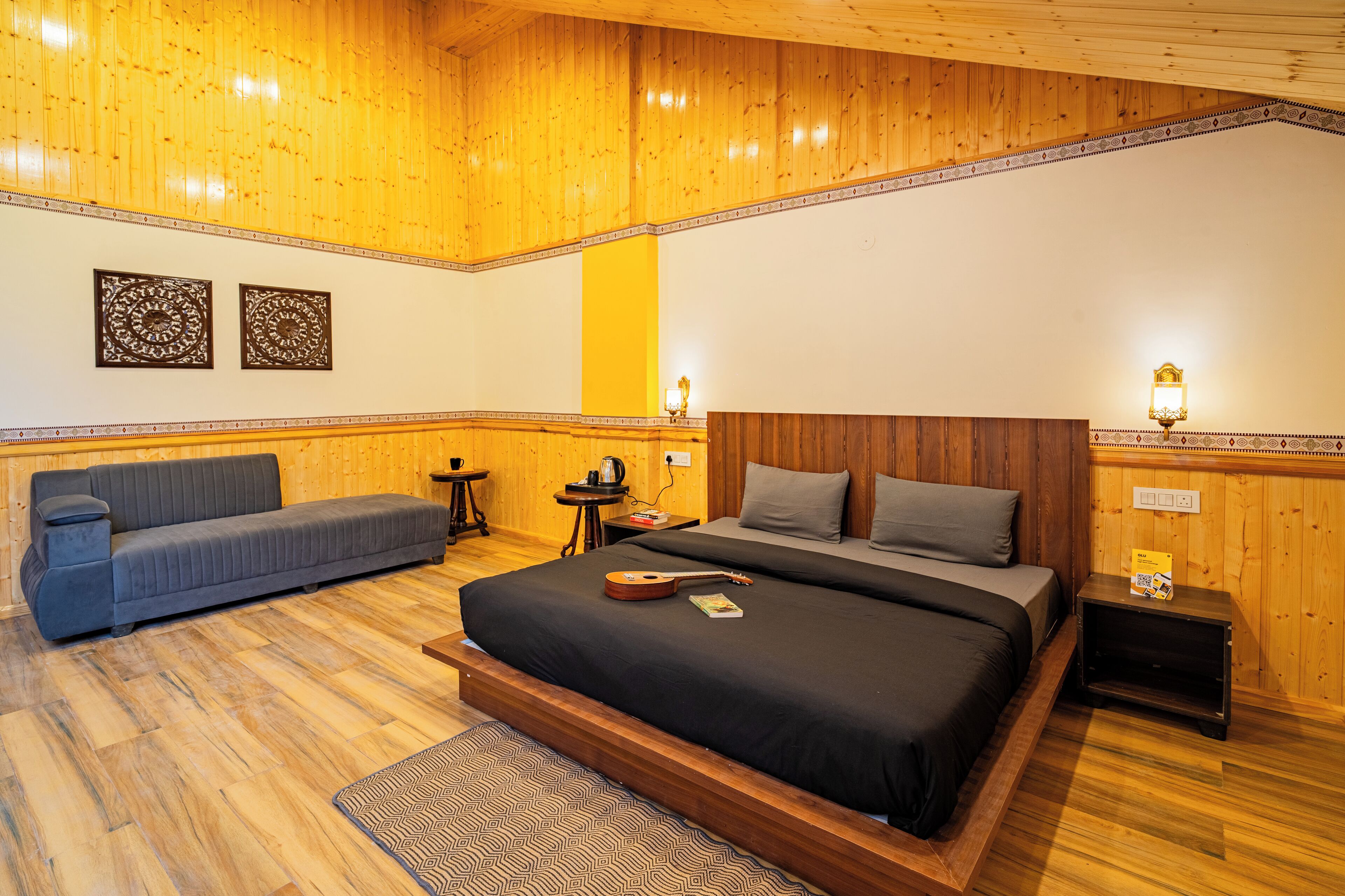 Une chambre avec un plafond en bois, un lit avec une guitare, un canapé, une petite table et deux lampes fixées au mur.