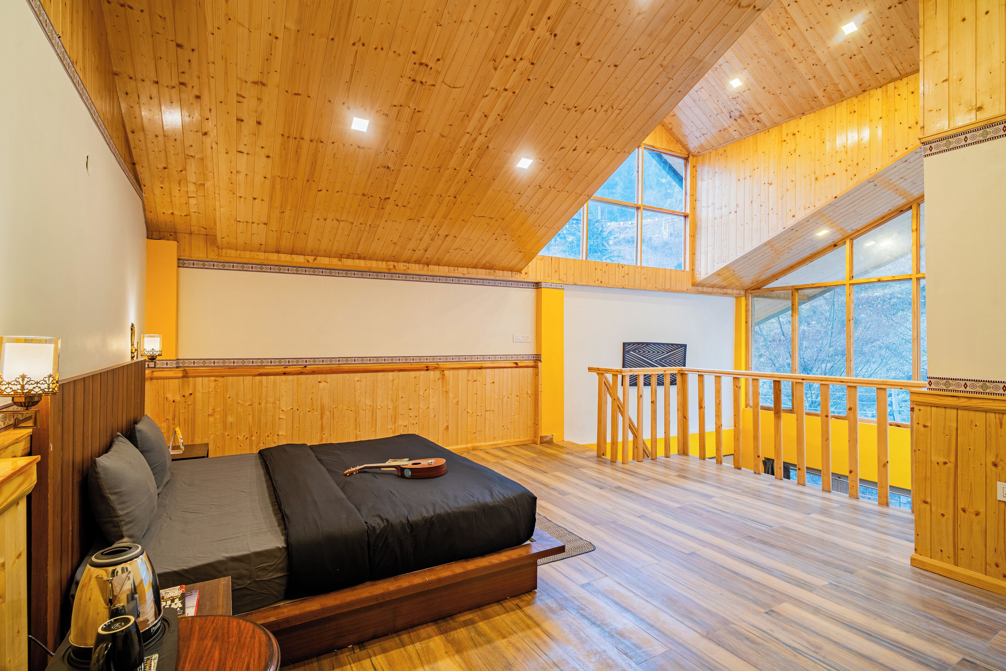 A spacious bedroom with a large bed, wooden ceiling, and a balcony with a railing.