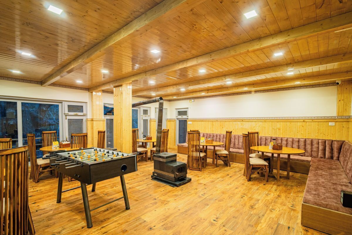 A cozy indoor space with wooden floors and walls, featuring a foosball table, a wood-burning stove, and comfortable seating areas.