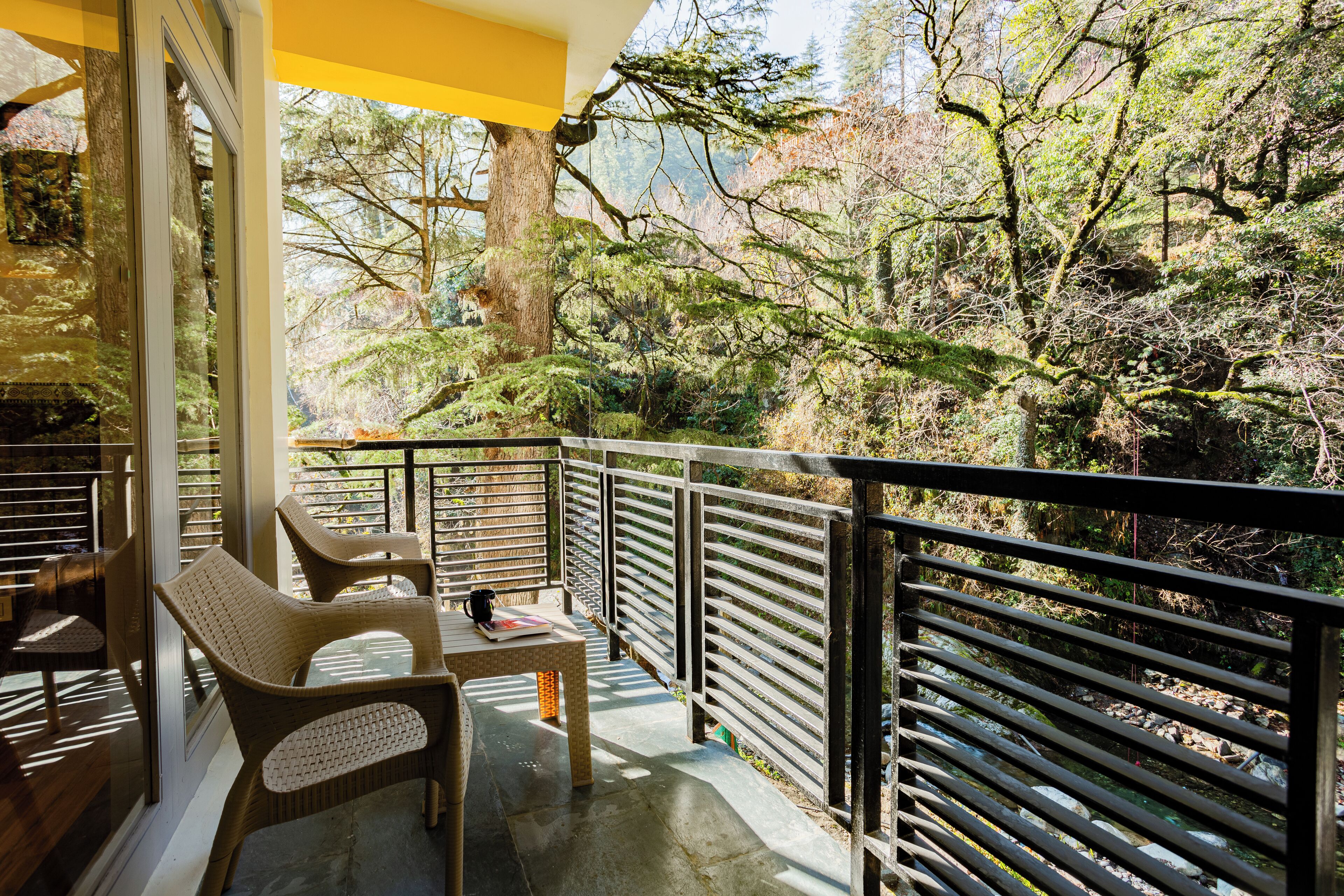A balcony with wicker chairs and a table, overlooking a forested area.