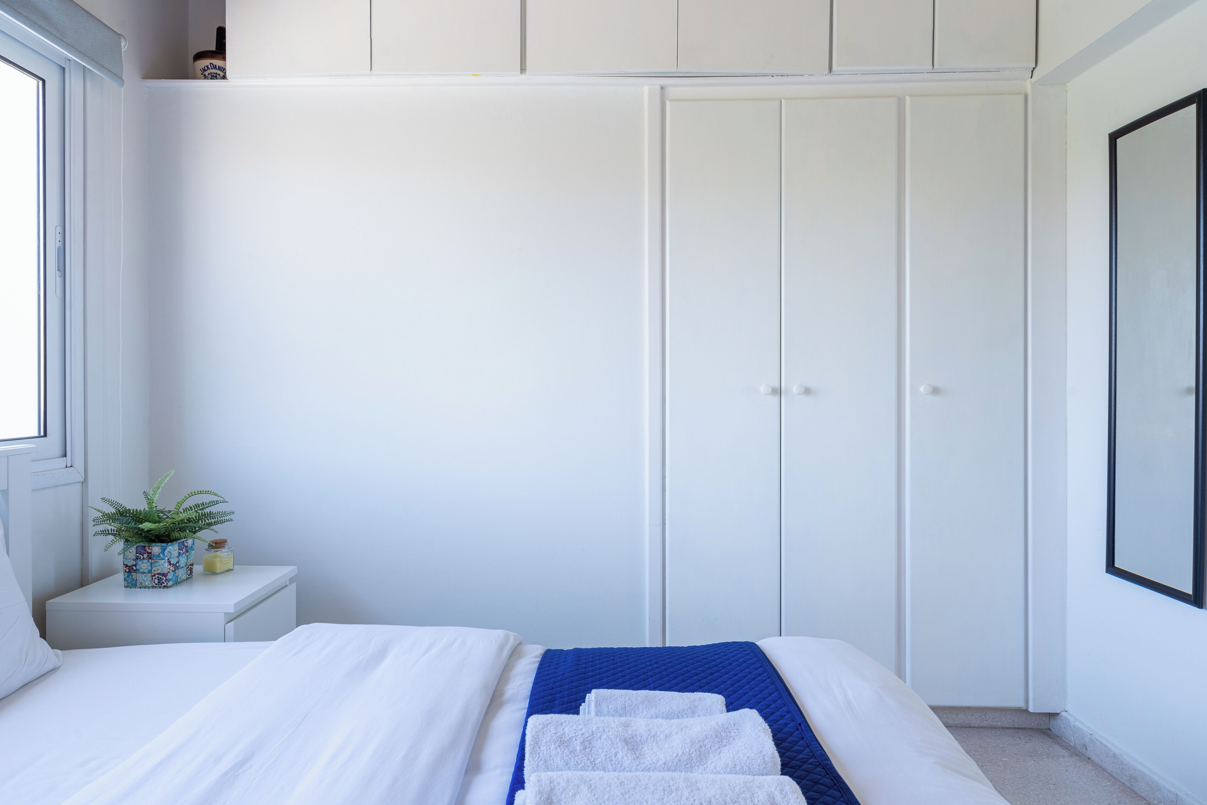 Ein Schlafzimmer mit einem Bett, einem Nachttisch mit Pflanze, einem Kleiderschrank und einem gerahmten Bild an der Wand.