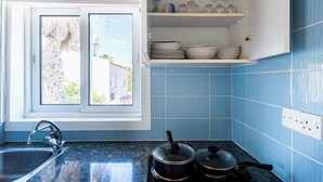 A kitchen with a sink, stove, and open cabinet with dishes. - Lazuli 1-BR W Pool & Balcony in Larnaca (Oroklini)