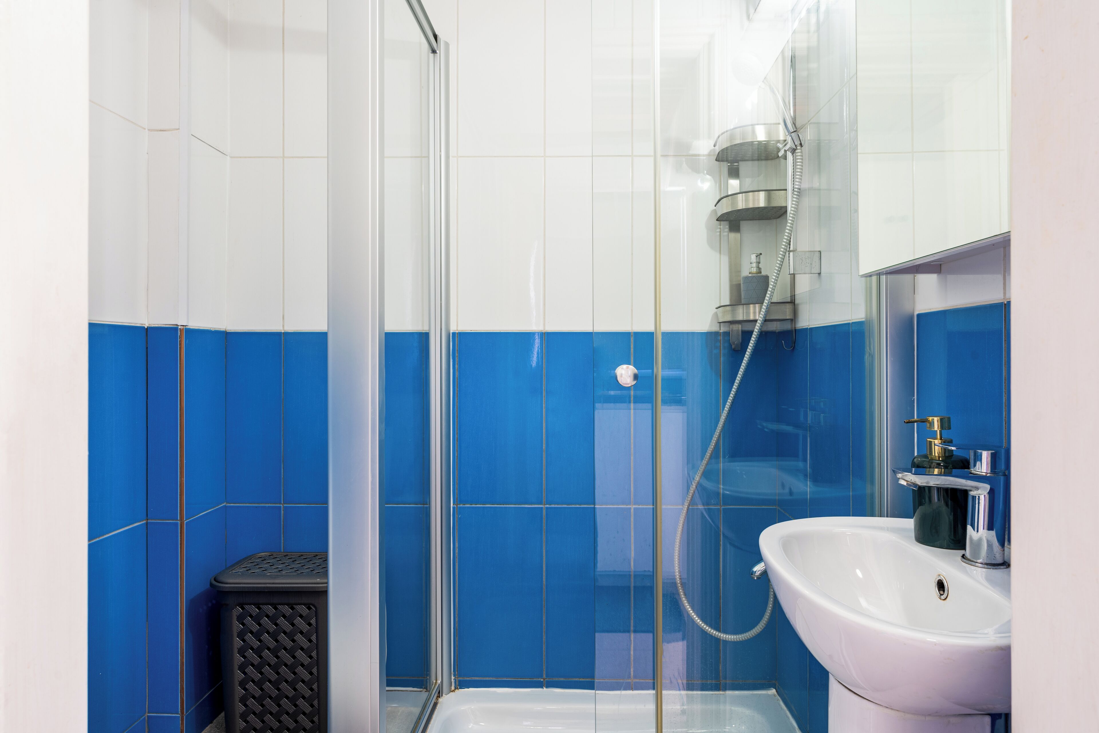 A bathroom with a glass-enclosed shower, a white sink, and blue-tiled walls.