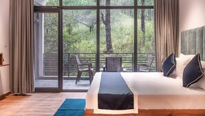 Un dormitorio con un ventanal grande, una cama, una alfombra azul y un balcón con sillas.