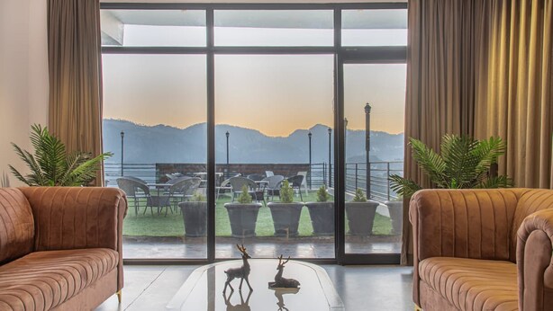 Una habitación moderna con un amplio ventanal corredera que da a un espacio exterior con vistas a las montañas. Hay dos sofás cómodos y una mesa de centro con figuras decorativas de ciervos.
