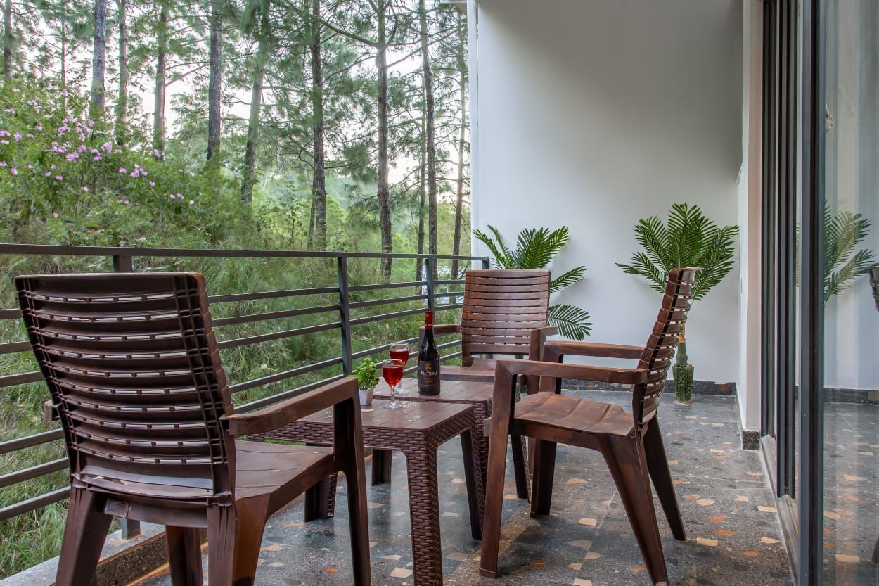 A balcony with two wooden chairs and a table, a bottle of wine, and a glass on the table.