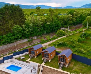Un resort con tres cabañas de madera, una piscina y vistas de la vegetación y montañas circundantes.