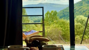 A table with two mugs and a telephone, a window with a view of green hills and a cloudy sky. - Sioni Hillside Cottages (Sioni)