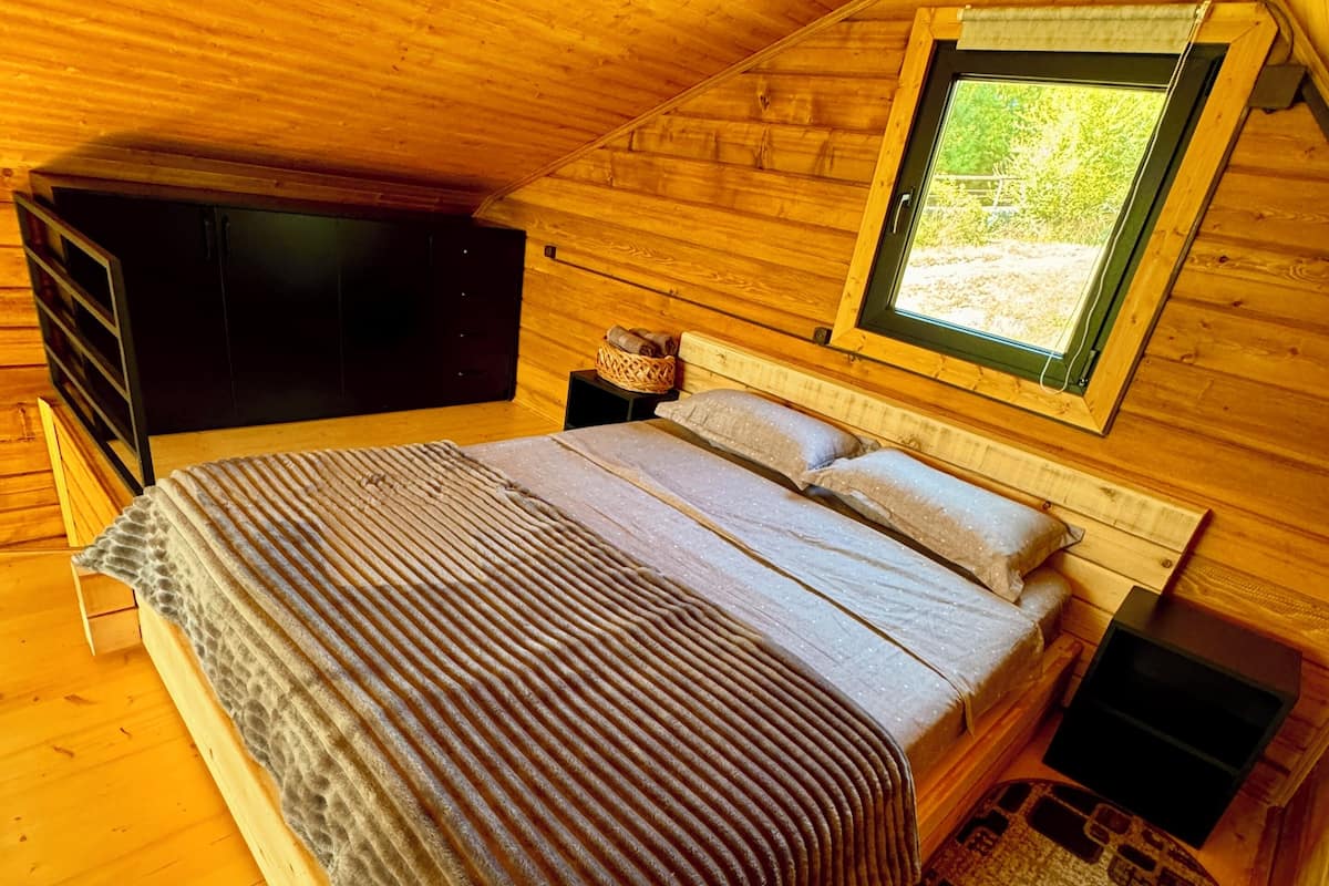 A cozy wooden cabin bedroom with a bed, a window, a TV, and a small table.