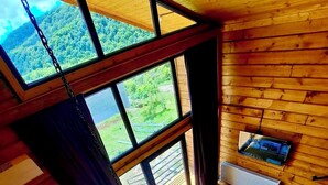 A high-ceiling room with large windows, a wooden floor, and a sofa with cushions. - Sioni Hillside Cottages (Sioni)