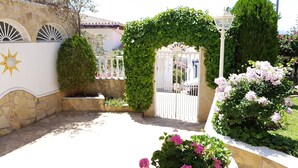 Un patio amurallado con un muro de piedra, un arco decorativo y plantas con flores.