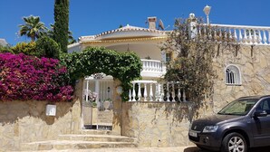 Un edificio de piedra con entrada porticada, un balcón y un coche estacionado.