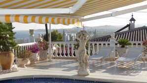Zona junto a la piscina con una estatua, sillones de descanso, plantas en macetas y vistas al mar.