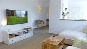 En moderne stue med et fladskærms-tv, en hvid sofa, et træbord og en fletstol.