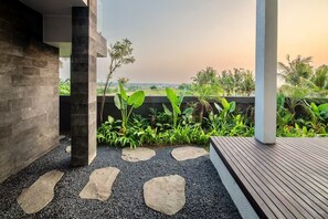 A modern outdoor patio area with a view of the landscape, featuring a stone pathway, wooden deck, and lush greenery. - Tranquil Luxury Stay with Rice-Field & Ocean Views, Private Pool+Bar, Chef & BBQ (Bali)