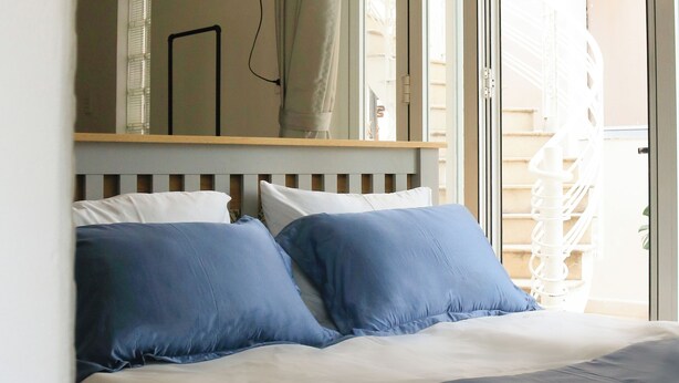 Un dormitorio con cama, lámpara colgante, ventana con cortinas y vista a una escalera.