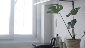 Una cocina con armarios blancos, encimera de granito, ventana con persianas y una planta en maceta.