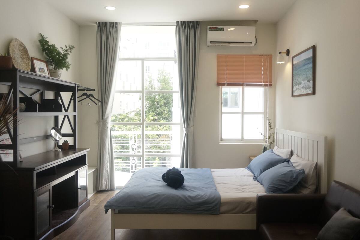 A bedroom with a bed, a dresser, a window with curtains, and a wall-mounted air conditioner.