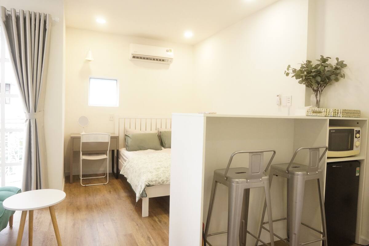 A compact room with a bed, a small table, a chair, a microwave, and a refrigerator.