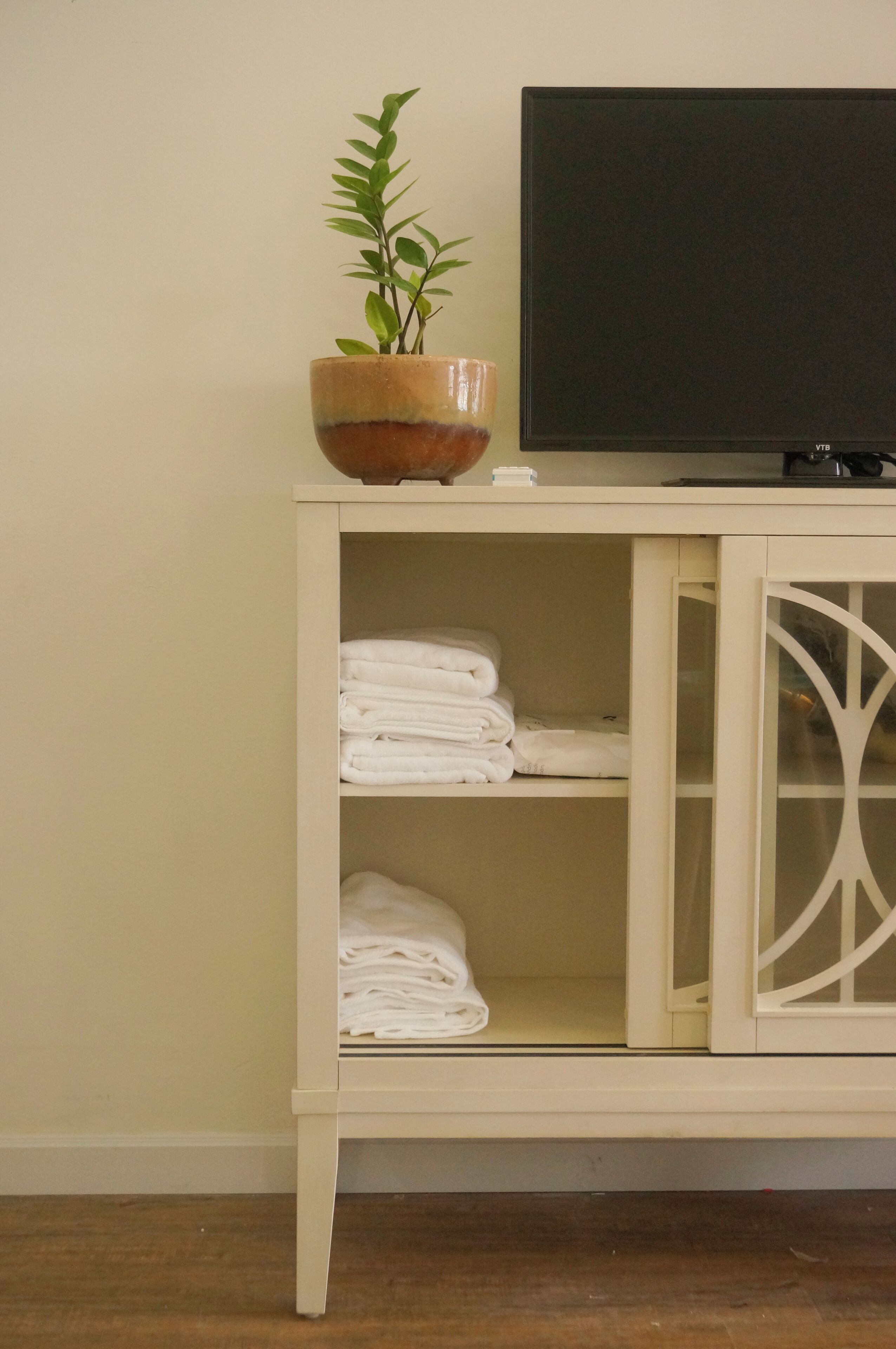 A white cabinet with a television on top and folded towels inside.