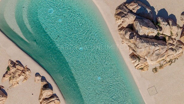 An aerial view of a beach with clear turquoise waters, rocky formations, and sandy areas. - Villa Tramas de Luna - Sardinia Unlimited (Capo Coda Cavallo)