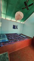 Una habitación pequeña con cama individual, techo de láminas verdes, ventilador de techo y una ventana con cortinas.