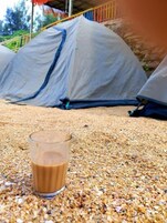 Una taza de café sobre un lecho de granos, con tiendas de campaña al fondo.