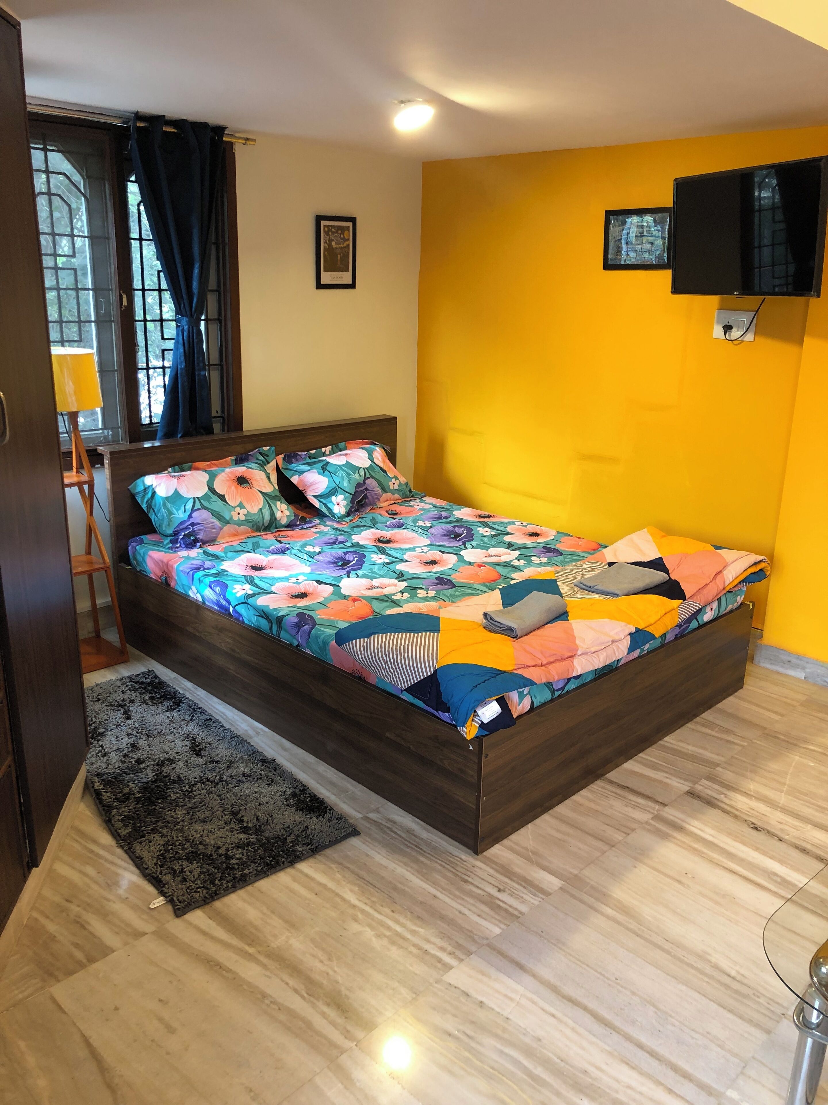 A bedroom with a wooden bed, floral bedding, a black rug, and a yellow wall.