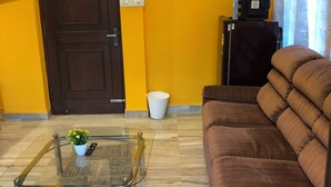 A living room with a brown sofa, a glass coffee table with a remote control, a small plant, and a patterned rug. - Cozy room The Hole In The Wall  (Bengaluru)
