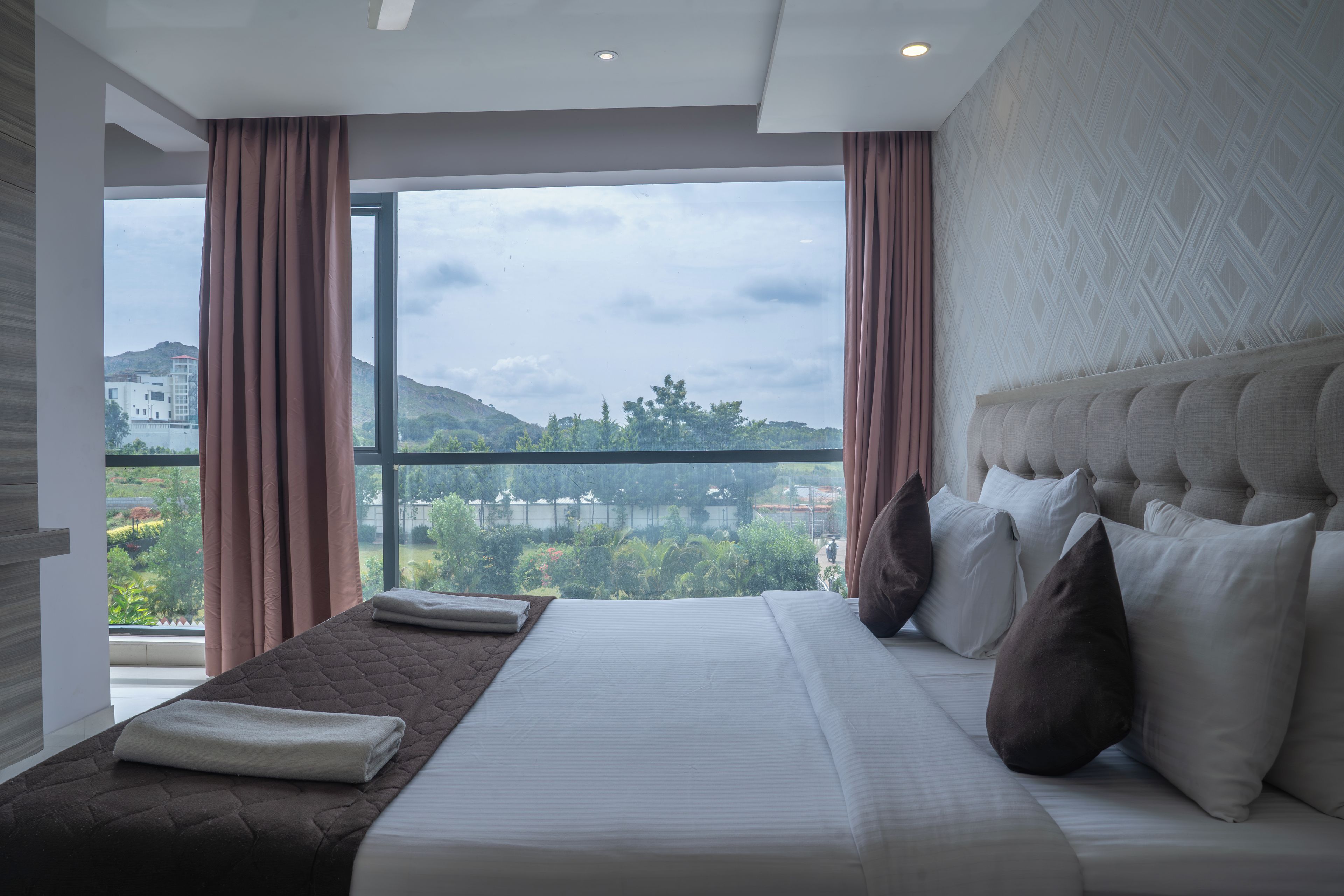 A modern hotel room with a large bed, a view of a cityscape, and a balcony.