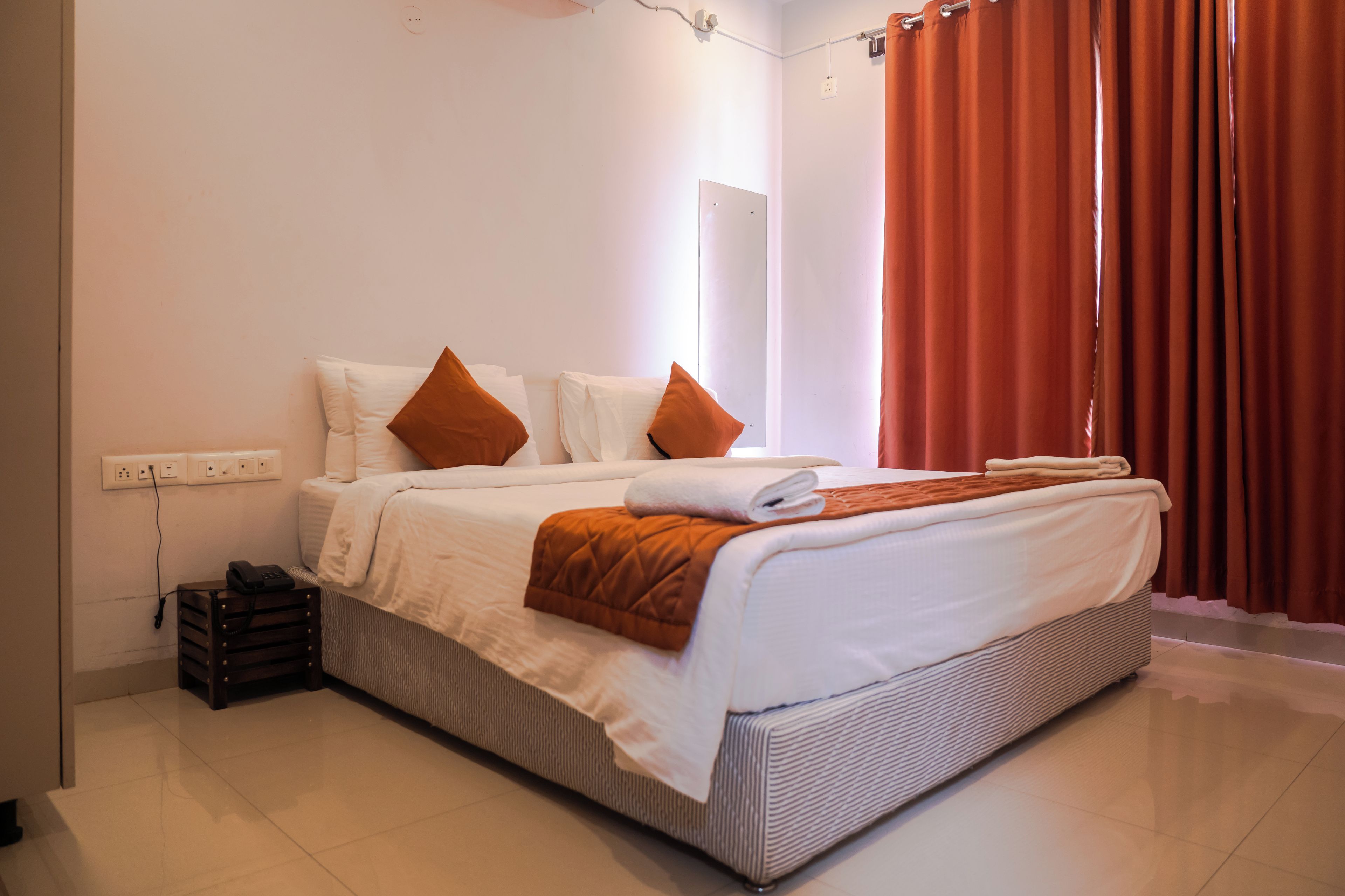 Ein Hotelzimmer mit einem Bett, Kissen, einer Decke, einem Telefon und einer Steckdose an der Wand.