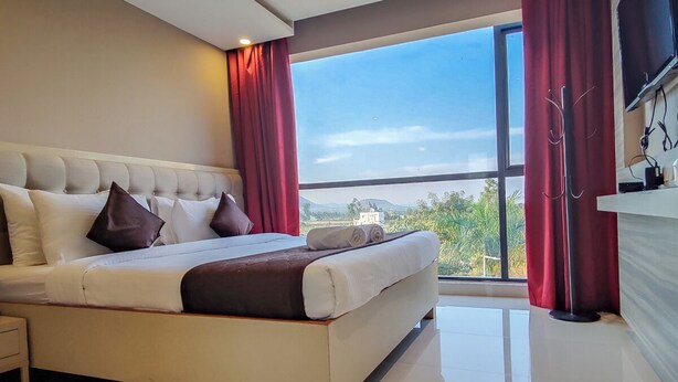 Een moderne hotelkamer met een groot bed, uitzicht op de omgeving en een flatscreen televisie aan de muur.