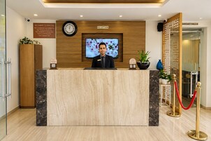 Un mostrador de recepción de hotel con un reloj, un televisor y un letrero que indica la zona de recepción.