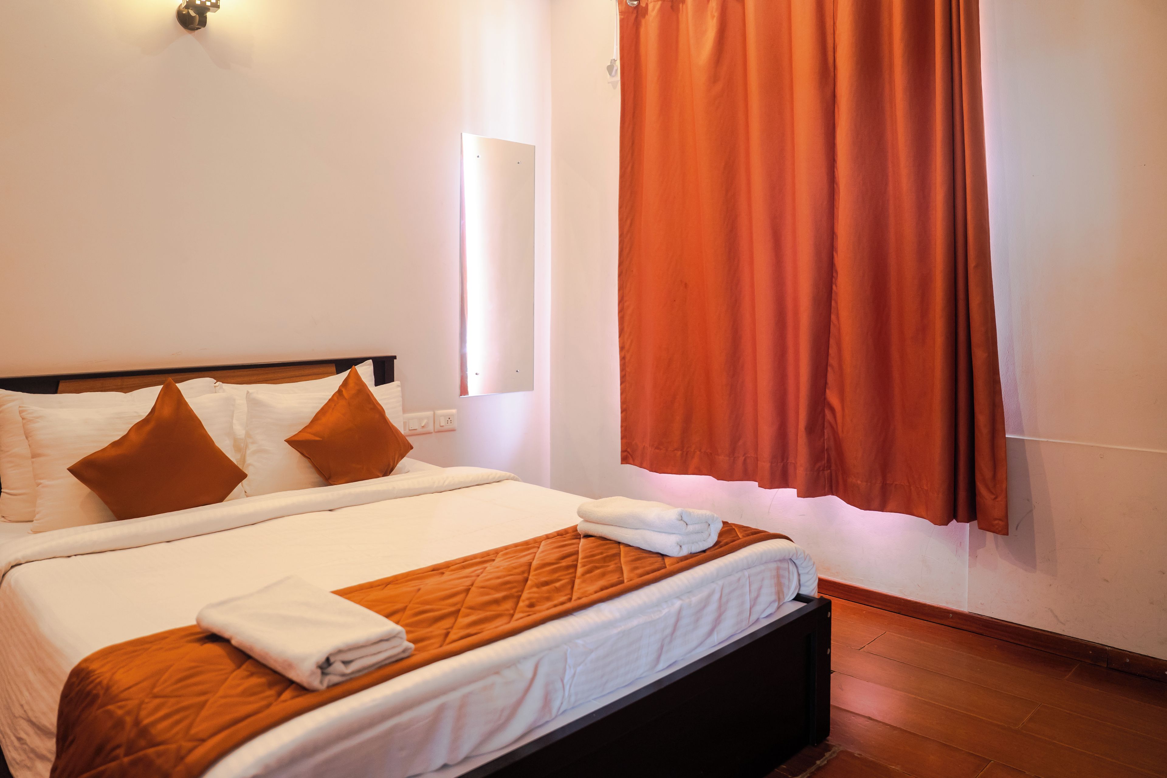A hotel room with a bed, pillows, a blanket, and a window with curtains.