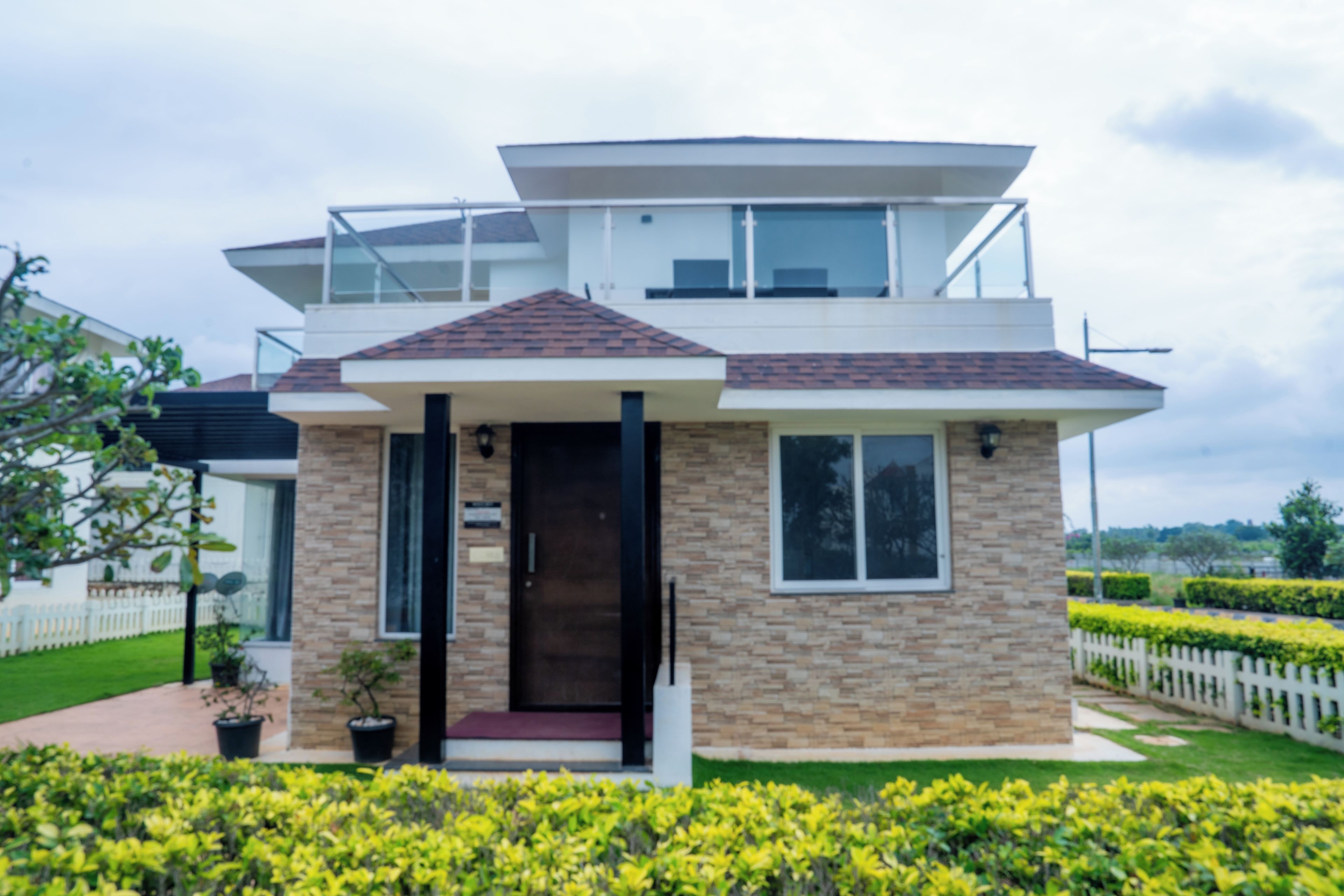 A modern two-story house with a flat roof, a balcony, and a front door.
