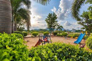 A playground with slides and climbing structures, surrounded by greenery and palm trees. - White Mist by NAVA (Devanahalli)