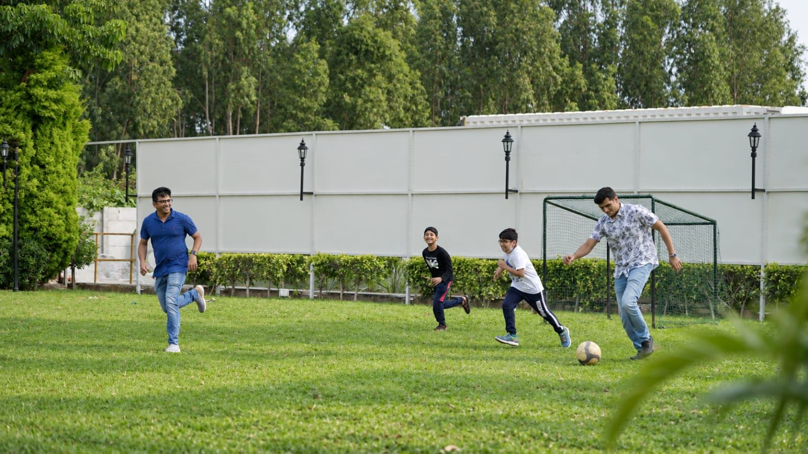 Eine grüne Wiese mit einem Fußballtor, Bäumen und einem Gebäude im Hintergrund.
